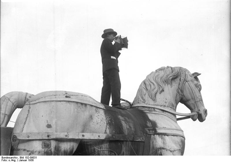 Berlin, Pressefotograf auf der Quadriga, Januar 1930 Originalbildunterschrift: „Die Jagd nach der Sensation, der Pressephotograph bei der Arbeit! Hoch zu Ross. Der Pressfotograf auf der Quadriga des Brandenburger Tors bei der Arbeit.“ Fotograf: unbekannt, Aktuelle-Bilder-Centrale, Georg Pahl (Bild 102), Quelle: Wikimedia Commons Bundesarchiv Bild 102-09031