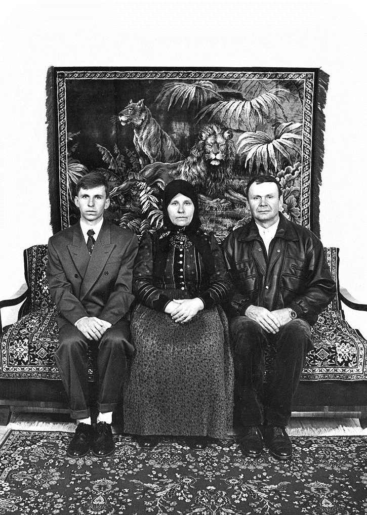 Familienporträt aus dem Jahr 1997: Der Ehemann, die Ehefrau und ihr Sohn posieren in der "guten Stube" ihres Hauses. Die Kleidung der Männer und der neue Wandteppich im Hintergrund weisen auf die Verdrängung des traditionellen, dörflichen Lebensstils hin. (Szék/Sic, Rumänien, 1997)