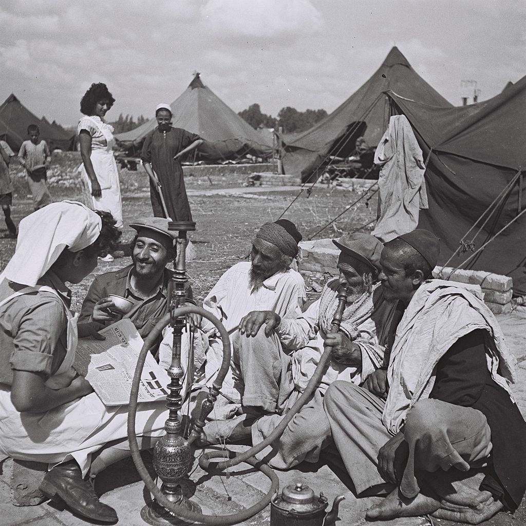 Zoltan Kluger (Foto): A young Yemenite nurse reading from a newspaper to new migrants at the Rosh Ha'ayin camp. Israeli National Photo Archive, 01.10.1949 Quelle: https://commons.wikimedia.org/wiki/File%3AYemenites_at_Rosh_Haayin.jpg Lizenz: Public domain